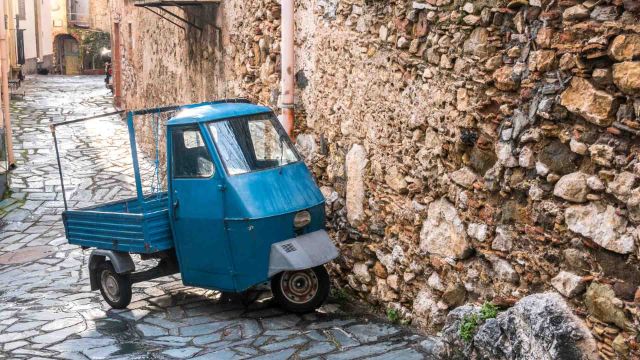 Italienische Ape Piaggio parkt an Steinmauer.