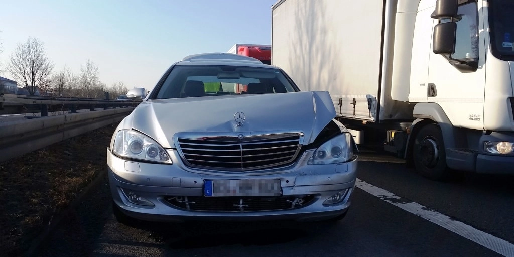 Silberner Mercedes auf Autobahn neben weißem Lastwagen mit Warnlicht auf Dach