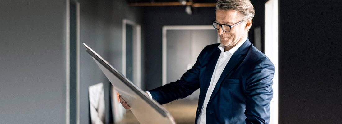 Geschäftsmann in dunklem Blazer und Brille betrachtet Baupläne in modernem Büro