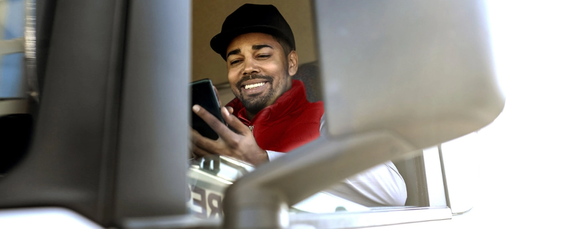 Truck-Fahrer im Truck, schaut auf sein Smartphone.