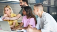 Familie sitzt zusammen am Tisch mit Laptop und bespricht Finanzen oder Schulaufgaben in der Küche.