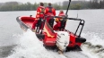 Rettungskräfte in roter Ausrüstung fahren mit Luftkissenboot durch Hochwasser auf breiter Wasserfläche