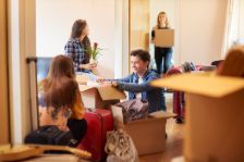 Eine Gruppe von vier Studenten zieht in ihre Wohngemeinschaft ein und beginnt, Kisten auszupacken. Ein männlicher Student sieht seine Kisten im Vordergrund durch.