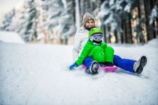 Eine Mutter sitzt mit ihrem Kind auf einem Rodelschlitten und fährt den schneebedeckten Abhang runter