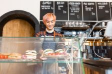 Junger Barista, der frisch zubereitete Speisen in der Auslage eines Cafés anrichtet.