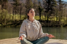 Frau im Trainingsoutfit sitzt am See und praktiziert Yoga.
