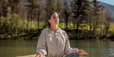 Frau im Trainingsoutfit sitzt am See und praktiziert Yoga.