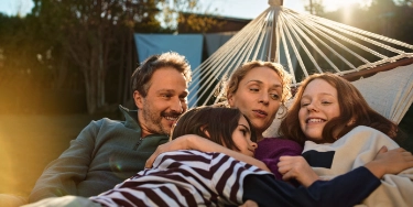 Eine Familie liegt gemütlich in einer Hängematte.