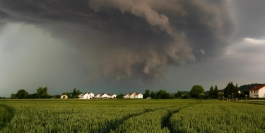 Gewitterwolken über flacher Landschaft mit Getreidefeld, Bauernhöfen und Häusern am Horizont
