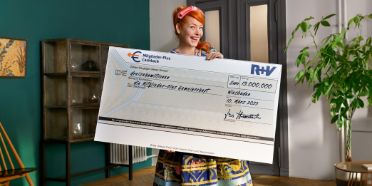 Enie van de Meiklokjes hält einen Scheck in der Hand über 13 Mio. EURO für die Mitglieder-Plus-Gemeinschaft der R+V Versicherung