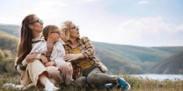 Drei Generationen sitzen zusammen in der Natur: Großmutter, Mutter und Tochter blicken zuversichtlich in die Zukunft..