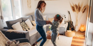 Mutter und Tochter springen gemeinsam im Wohnzimmer.