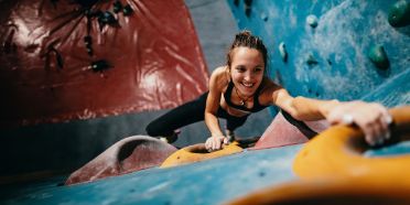 Frau klettert eine Indoor-Kletterwand hoch.