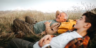 Großvater und Enkel leigen entspannt in einem Feld.