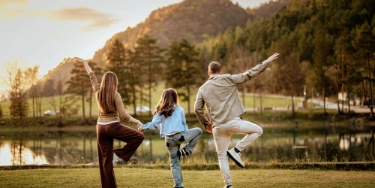 Familie macht Yoga im Freien, Mutter und Vater und Kind halten sich an den Händen.