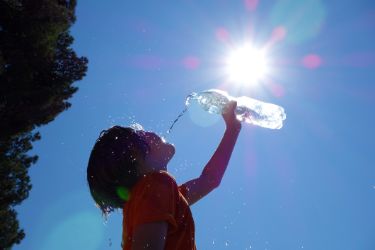 Kind trinkt aus Flasche bei Sonnenschein und Hitze