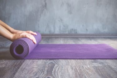Eine Frau rollt eine lila Yogamatte aus