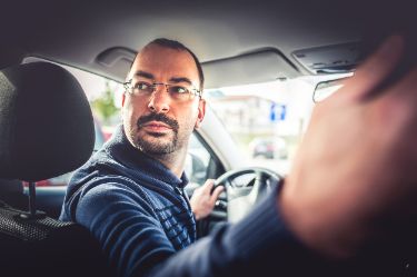 Mann faehrt rueckwaerts im Auto.