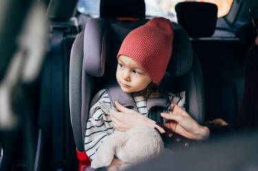 Ein keines Kind sitzt in einem Kindersitz im Auto und ist mit einer dicken Winterjacken angezogen.