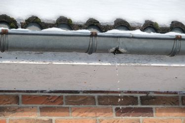 Undichte Dachrinne, unter einem verschneiten Dach.