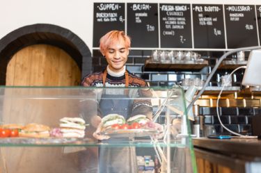 Junger Barista, der frisch zubereitete Speisen in der Auslage eines Cafés anrichtet.