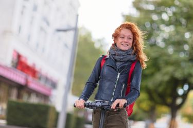 Eine Frau fährt auf einem eRoller in der Stadt.