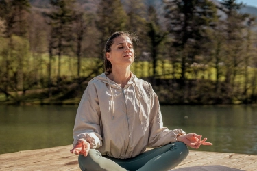 Frau im Trainingsoutfit sitzt am See und praktiziert Yoga.