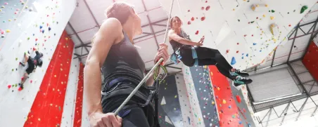 Zwei Frauen in einer Kletterhalle. Eine Frau sichert die andere. 