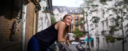 Junge Frau trinkt einen Kaffee auf ihrem Balkon in der Stadt.