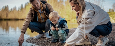 Familie mit Kleinkind spielen am Rande eines Sees mit dem Wasser.