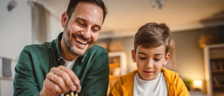 Vater und Sohn lachen zusammen in einem hellen Wohnzimmer, während sie auf einen Bildschirm schauen.