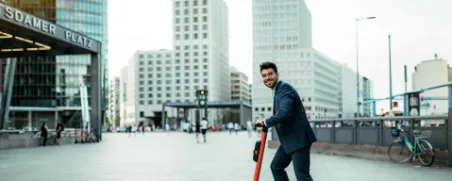 Ein Mann fährt im Anzug auf einem E-Roller durch die Stadt.
