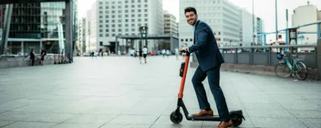 Ein Mann fährt im Anzug auf einem E-Roller durch die Stadt.