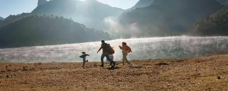 Eine junge Familie rennt fröhlich am Ufer eines Sees in den Bergen entlang.