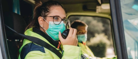 Arbeiter in Warnweste und Schutzbrille mit Atemmaske in Fahrzeugkabine, telefoniert.