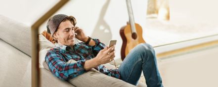 Junger Mann liegt bequem auf dem Sofa und schaut auf sein Smartphone.