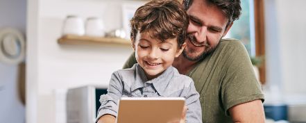 Vater und Kleinkind schauen auf ein Tablet.