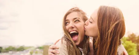 Lachende junge Frauen umarmen sich.