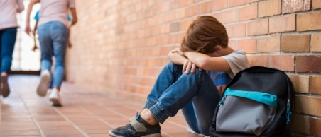 Kind sitzt allein und traurig auf dem Schulflur durch Stress bei Kindern RuV