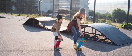 Zwei Skateboarder auf einem Skatepark vor Hochhäusern freuen sich, weil sie über die R+V Unfallversicherung abgesichert sind.