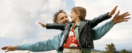 Vater und Tochter stehen mit ausgestreckten Armen auf einer Wiese als Symbol für finanzielle Freiheit durch IndexInvest.