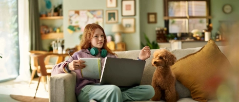 Ein junges Mädchen sitzt auf dem Sofa und erkundigt sich mit ihrem Computer über eine Berufsunfähigkeitsversicherung für Schüler.