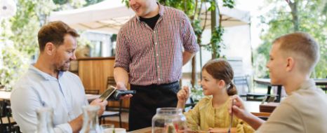 Ein Mann sitzt mit seiner Familie im Restaurant beim Essen und bezahlt die Rechnung.