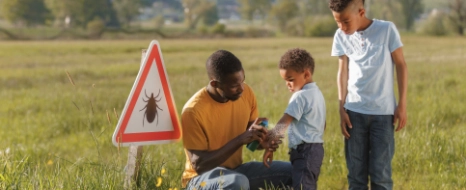 Ein Vater ist meinen Söhnen unterwegs und schützt sie mit Insektenspray vor Zecken.