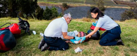 Ein Mann und eine Frau leisten Erste HIlfe bei einer Motorradfahrerin, die einen Unfall hatte.