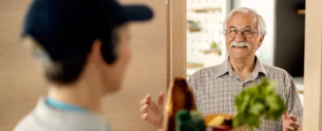 Ein junger Mann liefert einem aelteren Herrn in einer Papiertuete Lebensmittel