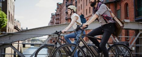 Zwei Personen fahren mit e-bike durch Stadt.