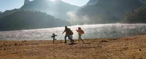 Eine junge Familie rennt fröhlich am Ufer eines Sees in den Bergen entlang.