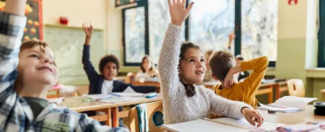 Schüler sitzen an ihren Tischen in der Schulklasse und melden sich eifrig im Unterricht.