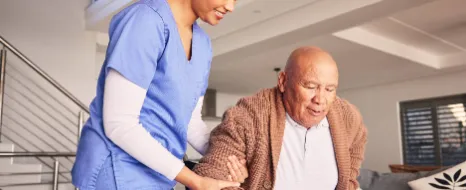 Eine Pflegerin hilft einem Senior aufzustehen.